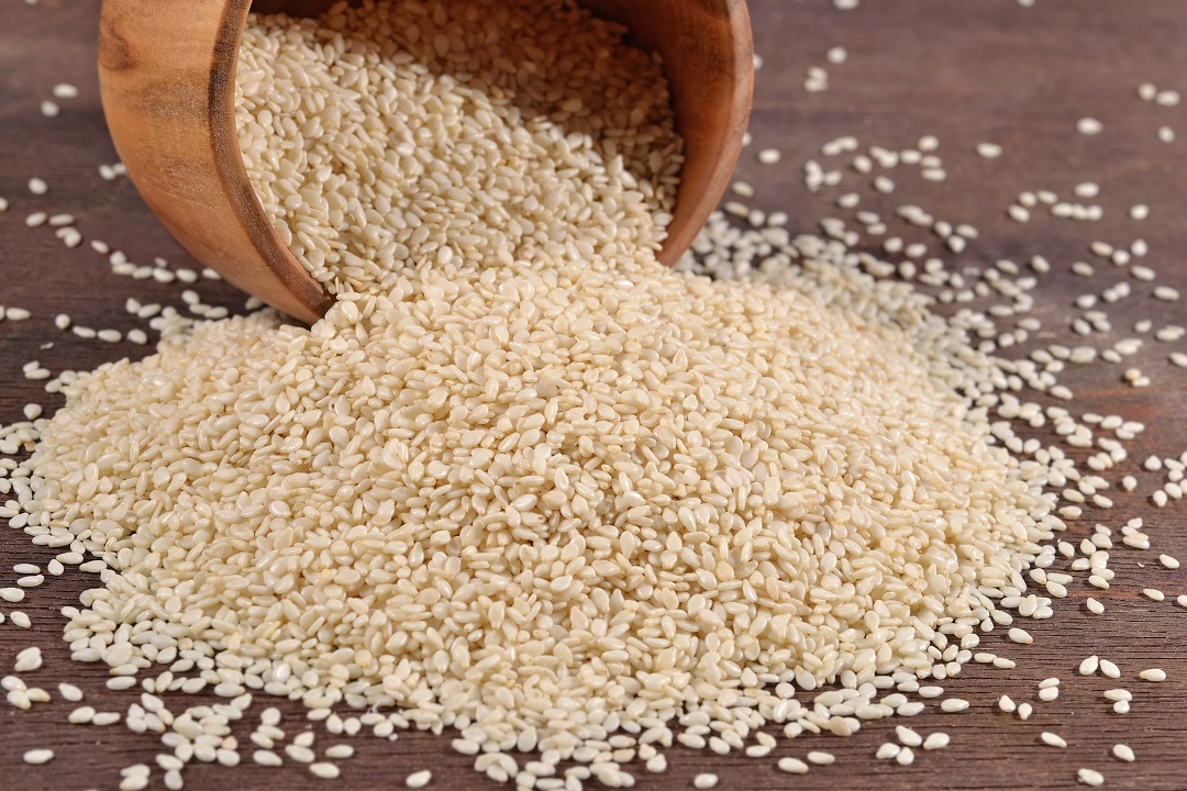 Sesame seeds spilling out ofa wooden bowlonto a wooden table.