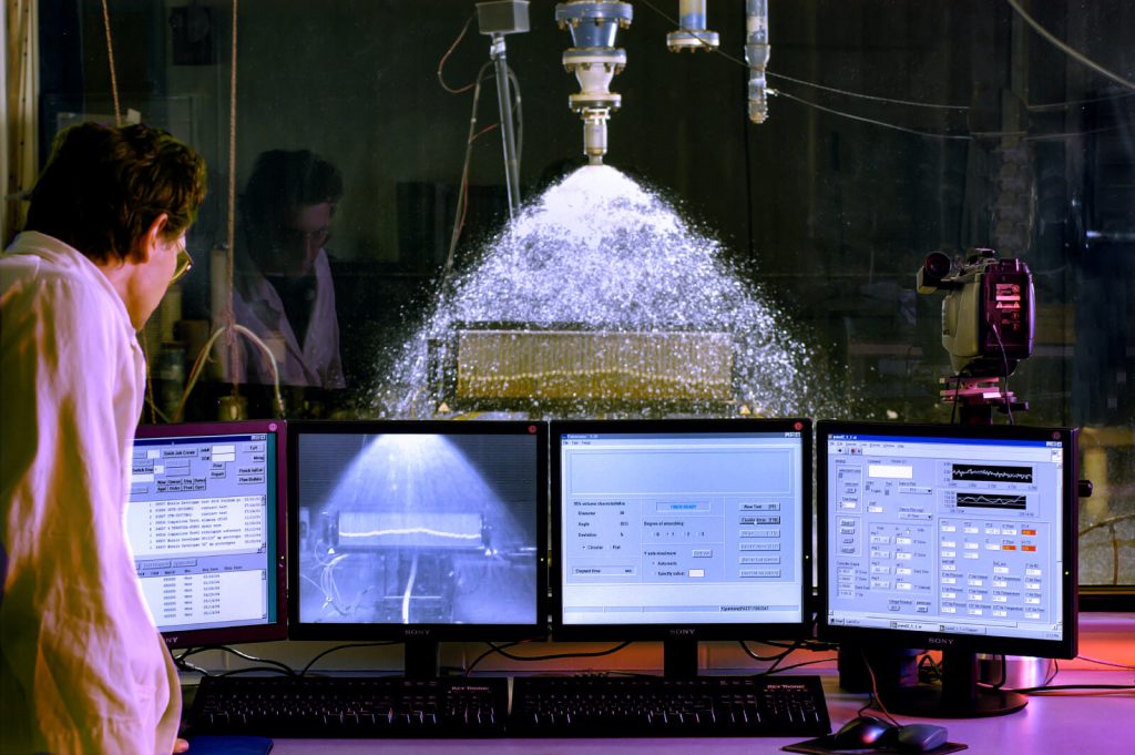 a man stands in front of computer monitors while testing a spray nozzle