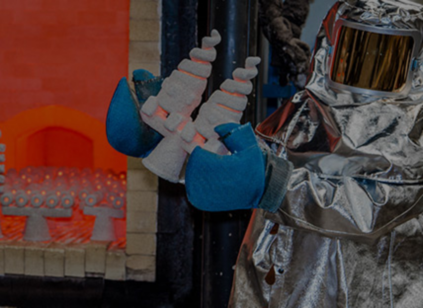 A man dressed in fire proof suit taking a nozzle out of a furnace.